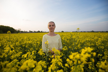 Fototapeta premium Happy woman on blooming rapeseed field in springin yellow blouse.