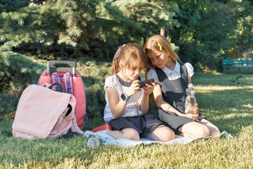 Two little schoolgirls using smartphone. Children playing, reading, looking at the phone.