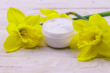 Obraz na płótnie Canvas Jar of moisturizer cream with yellow daffodils on white wooden background
