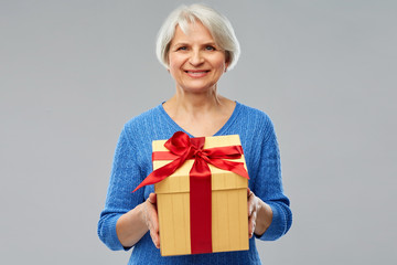 holidays, old age and people concept - happy smiling senior woman with gift box over grey background