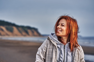 Portrait of a laughing middle-aged woman with red hair walking along the river bank. Sunny spring morning. Close-up.