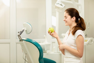 Female dentist smiling and holding a green apple, dental care and prevention concept