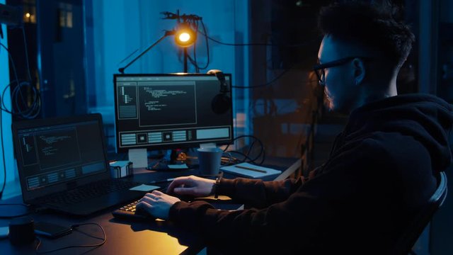 cybercrime, hacking and technology concept - asian male hacker in glasses writing code or using computer virus program for cyber attack and drinking coffee in dark room at night