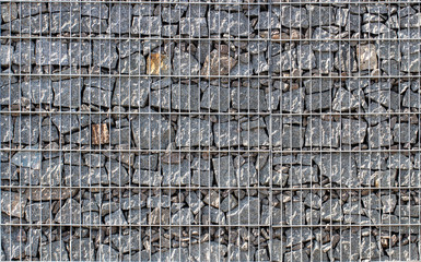 Gabion, a stone wall with a metal grid of gray granite texture