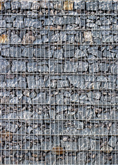 Gabion, a stone wall with a metal grid of gray granite texture
