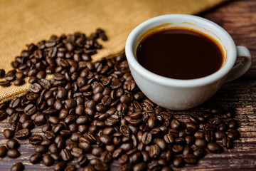 Cup of coffee with beans on wooden background