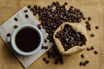 Top view a cup of hot coffee, coffee beans on sack background