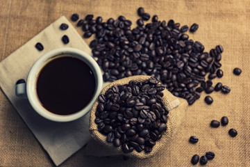 cup of coffee and coffee beans in a sack, top view