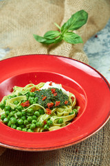 Spaghetti with fresh green peas. Gray textured background with beige fabric. Beautiful serving of dishes. Restaurant menu