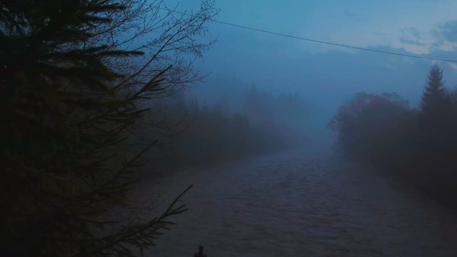 Mountain river in the fog in the dark. Rainy sky above the water. Haze over the forest river. 4k