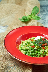 Spaghetti with fresh green peas. Gray textured background with beige fabric. Beautiful serving of dishes. Restaurant menu