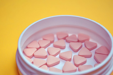 Pink triangular unusual pills in a white round box on yellow background with copyspace, side view closeup