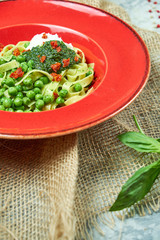 Spaghetti with fresh green peas. Gray textured background with beige fabric. Beautiful serving of dishes. Restaurant menu