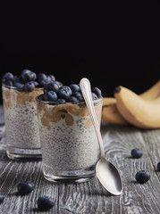 Chia with banana and blueberries in glass with spoon and banana on wooden table