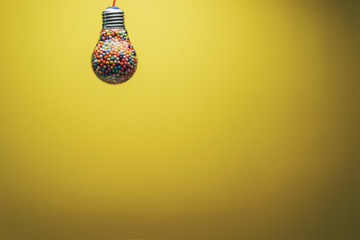 Creative lightbulb filled with multi colored ball on a yellow background behind. Best idea concept.