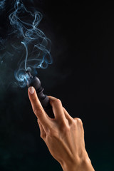 Hookah mouthpiece with a stream of smoke in a beautiful female hand on a dark background. Copy space.