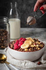healthy breakfast granola in a plate with nuts, banana and raspberries, copy space