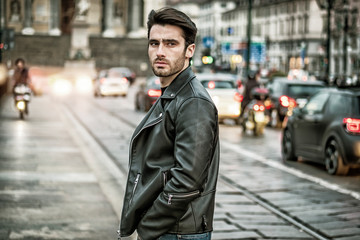One handsome young man in urban setting in modern city, standing, wearing black leather jacket and...