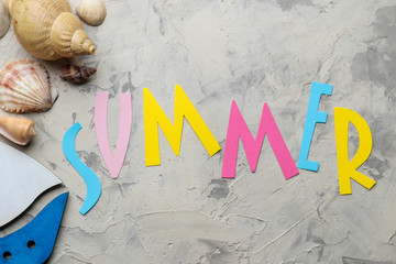 The word summer from paper with multicolored letters and sea accessories, shells on a light concrete background. summer. vacation. relaxation. top view