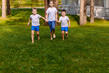 Obraz premium Two boys and a ten-year-old girl running on the green grass. Happy smiling kids in summer