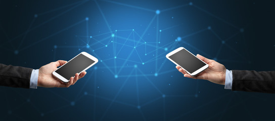 Close up of two hands holding smartphones to each other, wireless connection concept