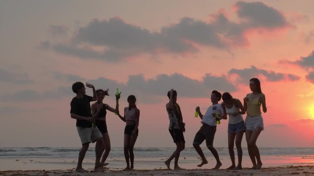 Silhouette of Asian teen group dancing and drinking beverage together in beach summer with sunset background. Young asia happy emotion and anniversary celebration. 4K resolution and slow motion.