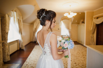 young beautiful wedding bride stands in a bright room in the apartment and holds in her hands a wedding bouquet