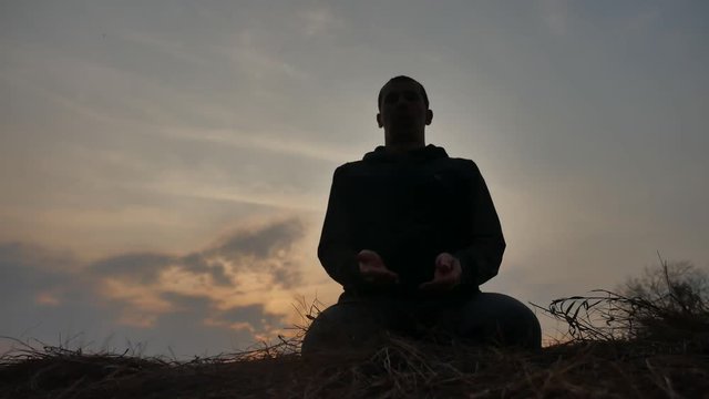 religion concept. silhouette of a male monk engaged in meditation at sunset lifestyle sunlight. Buddhist prayer at sunset healthy way of life nature