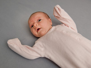 Infant baby is laying on grey background.