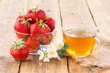 Glass cup of green tea and red ripe strawberries in glass bowl.