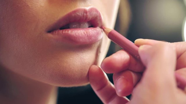 partial view of makeup artist applying beige lip pencil on model lips