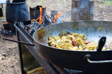 Potatoes with sausages fried in a pan on the coals in nature