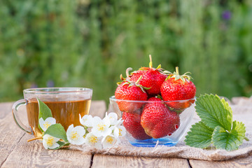 Glass cup of green tea and red ripe strawberries in glass bowl.