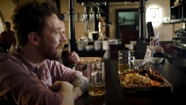 Cheerful friends drinking draft beer and eating snacks in a pub
