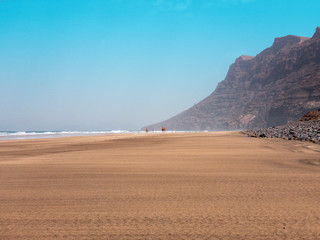 People walking on the Famara seafront, beach and mountains overlooking the ocean. Lanzarote, Canary Islands, Spain. Africa