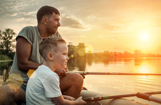 Happy Father And Son Together Fishing From A Boat At Sunset Time