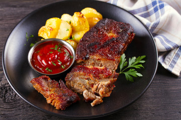 Grilled pork spare ribs with fries on black plate. Roasted sliced barbecue ribs
