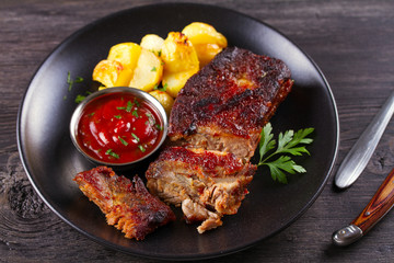 Grilled pork spare ribs with fries on black plate. Roasted sliced barbecue ribs
