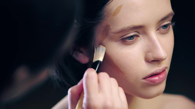 makeup artist doing contouring on model face with dark face foundation and cosmetic brush