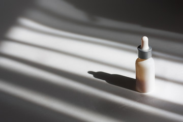 White serum bottle with yellow fillings  on grey shadowed background. Concept beauty composition, concept skin treatment