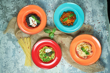 Multi-colored plates with pasta. Gray light textured background. Beautiful serving of dishes. Restaurant menu