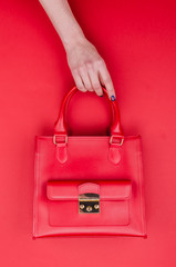 Bright summer fashion ladies accessories. Stylish red leather handbag or flap bag on a red background. Women hands with bright manicure holding bag from top. Top View. Flat Lay. Copy Space.