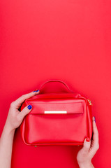 Bright summer fashion ladies accessories. Stylish red leather handbag or flap bag on a red background. Women hands with bright manicure holding bag. Top View. Flat Lay. Copy Space.