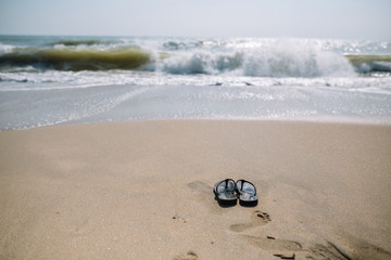 Fototapeta na wymiar Flip flops on a sandy beach in Summer vacation with waving sea.