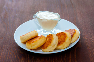 Fried cheese pancakes with sour cream on white plate on dark wooden background. For cafe or restaurant menu design.