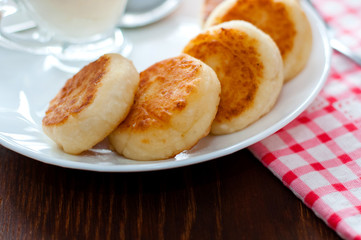 Cheese pancakes with sour cream on a white plate close-up. Can be used for menu design, culinary sites.