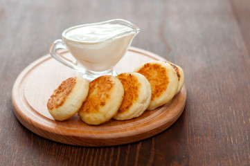 Cheese pancakes with sour cream on a wooden board, horizontal format. For menu design and cafe advertising