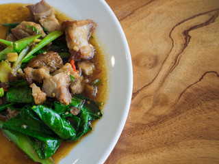 Stir-fried kale vegetable with crispy pork in white plate, Thai style fast food.