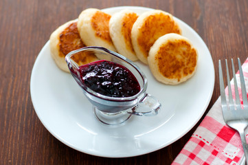 Cheese pancakes with currant jam, on a white plate with a fork, a teaspoon and a napkin, view from the top.