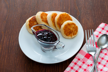 Cheese pancakes with jam, on a white plate with a fork, a teaspoon and a napkin, horizontal format